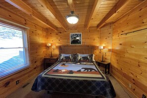A wooden cabin bedroom with a bed, two bedside tables, a window with blinds, and a ceiling light. - Mountain View Retreat 🏔️ Private Hot Tub, Arcade Room, Steps to Pigeon Forge Fun (Pigeon Forge)