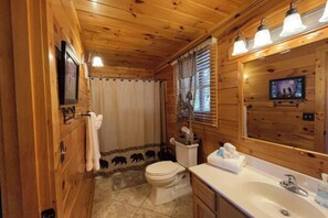 A wooden-paneled bathroom with a toilet, sink, and mirror. - Mountain View Retreat 🏔️ Private Hot Tub, Arcade Room, Steps to Pigeon Forge Fun (Pigeon Forge)