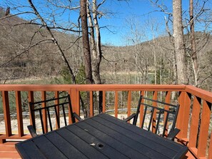 A wooden deck with a table and chairs, overlooking a forested area.