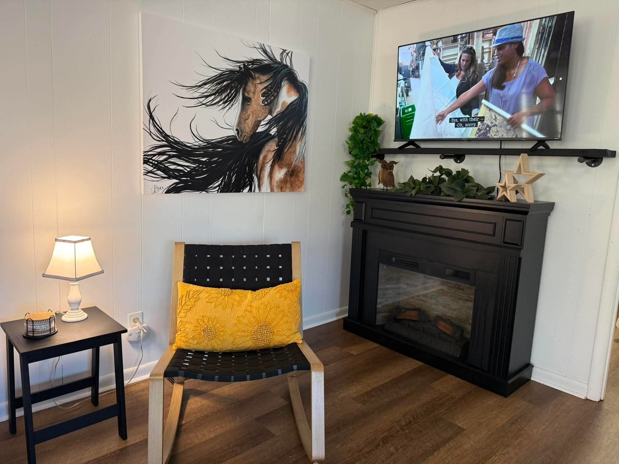 Ein Wohnzimmer mit einem schwarzen und gelben Sessel, einem an der Wand befestigten Fernseher, einem kleinen Tisch mit einer Lampe und einem Kamin.