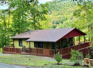 A single-story cabin with a porch, surrounded by a forested area.