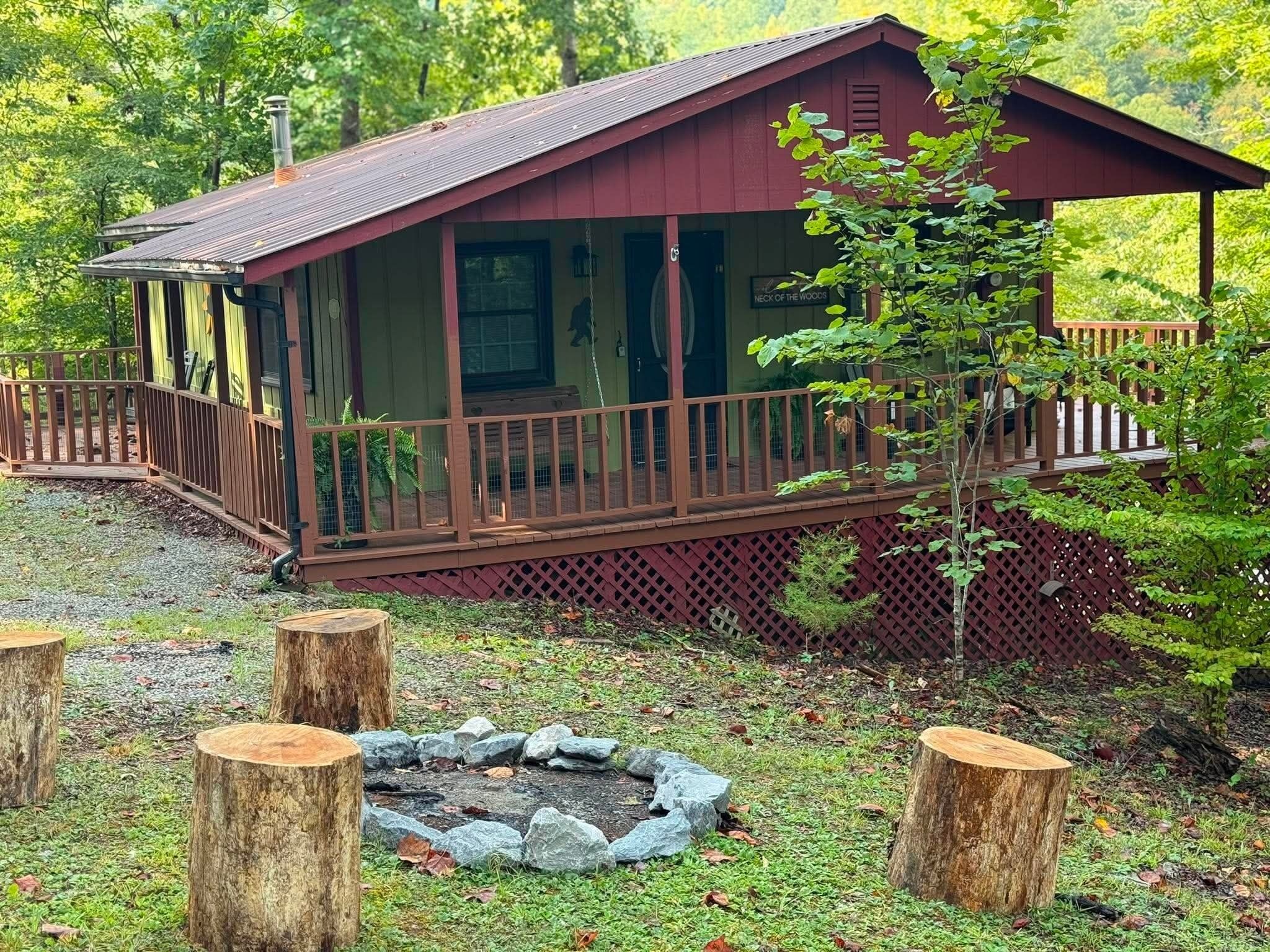 A cabin with a wooden deck, a covered porch, and a fire pit surrounded by rocks.
