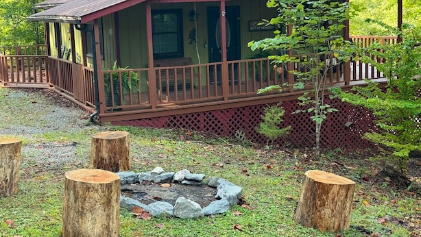 Eine Holzhütte mit einer Holzdiele, einer Veranda und einer Feuerstelle, umgeben von Steinen.