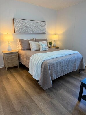 A bedroom with a bed, two bedside tables, a wall-mounted artwork, and a nightstand with a lamp.