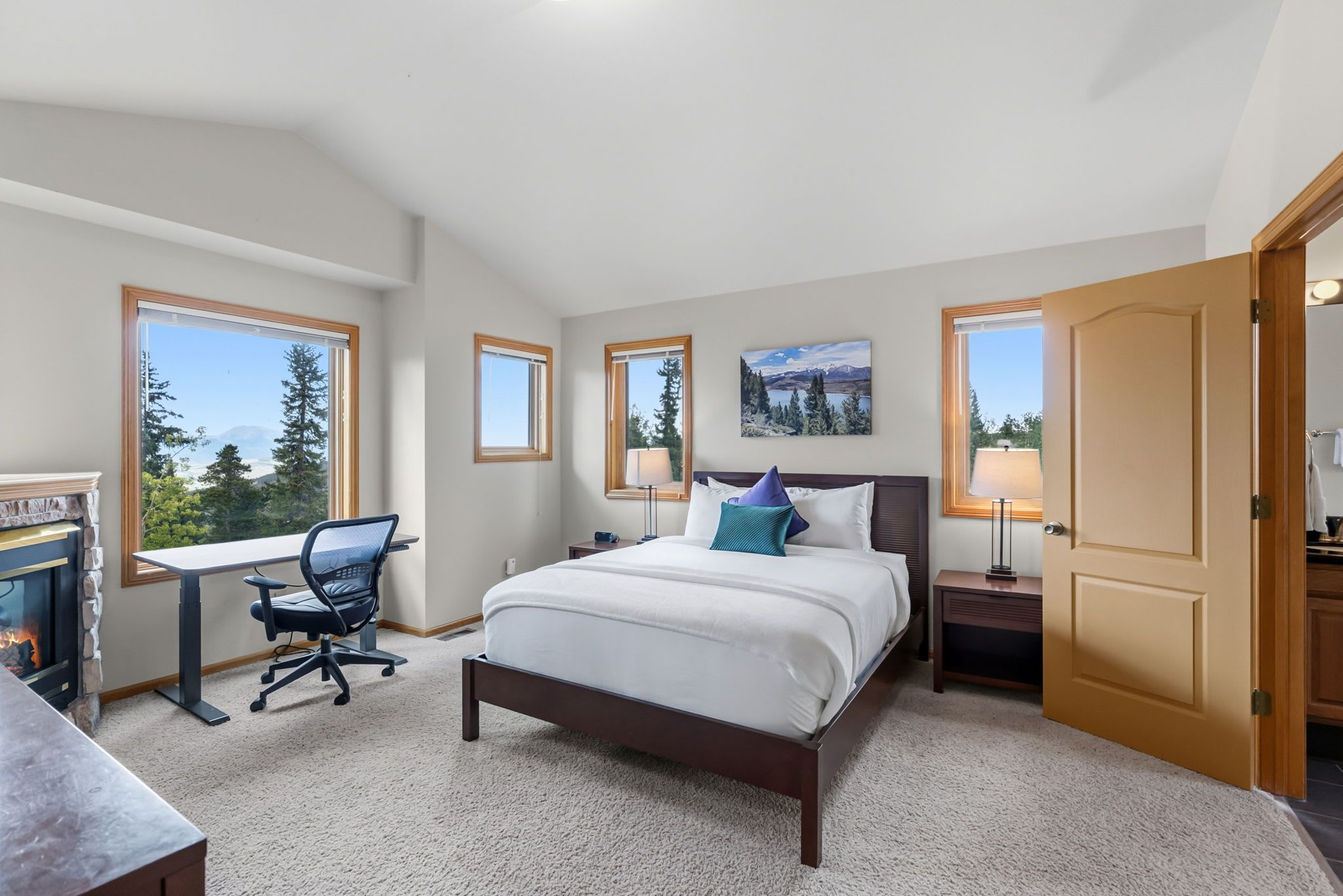 A bedroom with a bed, desk, chair, and a fireplace.