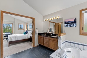 A hotel room with a bed, a bathroom with a sink and mirror, and a view of trees through the window. - First Light Cabin Breck - Deck & Views (Breckenridge)