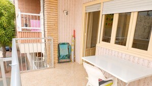 Ein Balkon mit einem weißen Tisch und Stühlen, einem kleinen grünen Sessel und einem Fenster mit Jalousien.