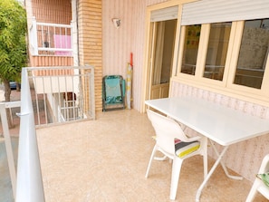 Un balcón con una mesa y sillas blancas, una silla verde pequeña y una ventana con persianas.