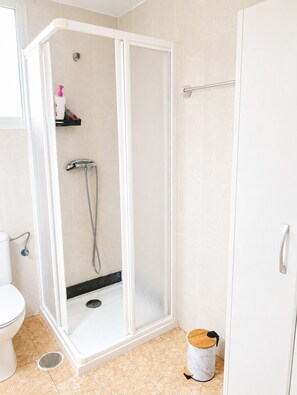 Un baño moderno con ducha envuelta en vidrio, inodoro y cubo de basura.