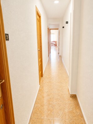 En hall med en trädörr på vänster sida, ett klinkergolv och utsikt över en matplats med stolar och ett bord.