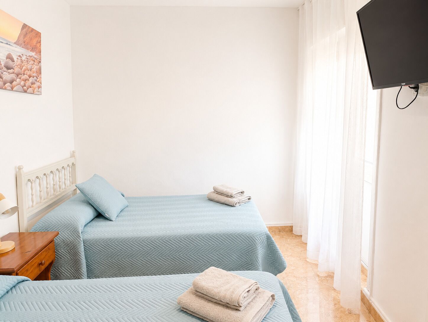 A hotel room with two beds, a flat-screen TV mounted on the wall, and a painting on the wall.