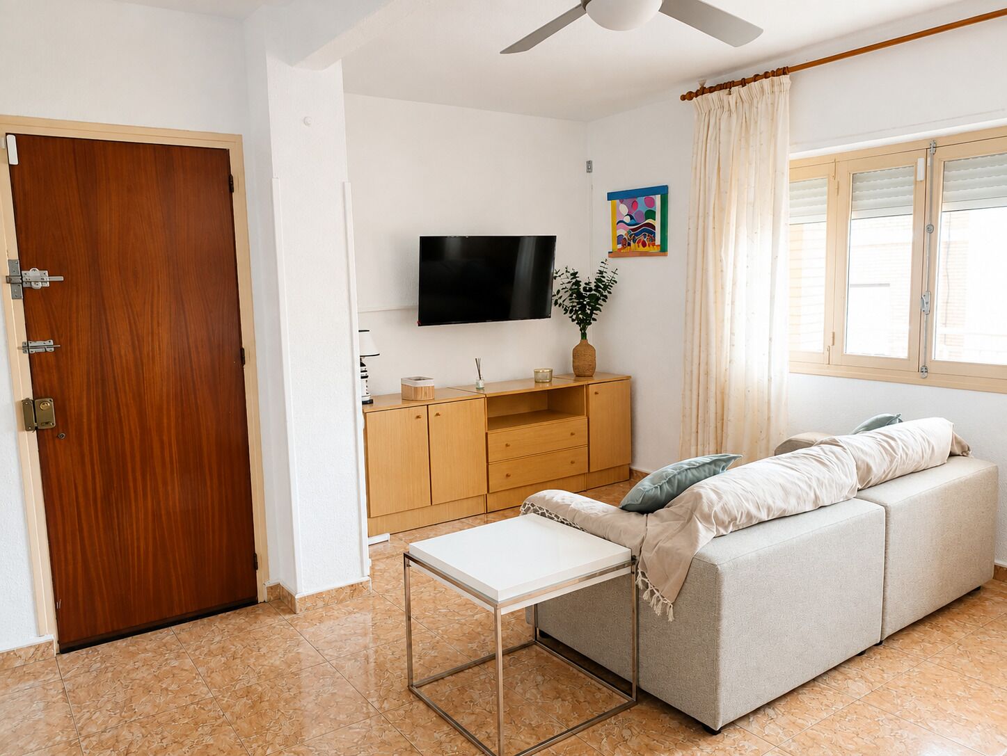 Una sala de estar con un sofá, un televisor, un aparador de madera y una mesita.