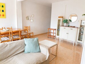 A living room with a sofa, a dining table with chairs, a small wooden side table, a cabinet with glass doors, and wall-mounted mirrors. - Beachfront Apartment in Los Alcázares - Murcia (Los Alcázares)