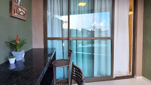 En balkon med glasdør, to fletstole, en marmorbordplade og en lille potteplante.