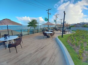 An outdoor seating area with tables and chairs, overlooking a beach. - Studio beira-mar nas piscinas naturais Tamandaré (Tamandaré)