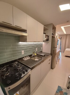A modern kitchen with a gas stove, stainless steel appliances, and a tiled backsplash. - Studio beira-mar nas piscinas naturais Tamandaré (Tamandaré)