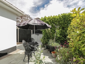 Eine Terrasse mit Tisch, Stühlen, Sonnenschirm und Kübelpflanzen.