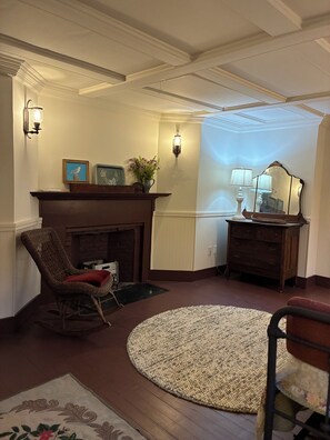 Un salon avec une cheminée, un fauteuil à bascule, un tapis rond et un miroir.