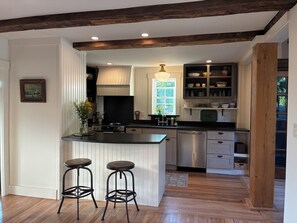 Une cuisine moderne dotée d’un îlot central, de tabourets de bar, d’appareils électroménagers en acier inoxydable et de poutres en bois au plafond.