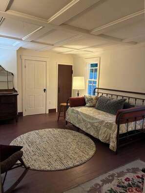 Une chambre à coucher avec un lit, une chaise, une lampe, une commode et une porte.