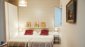Une chambre d’hôtel avec deux lits, une petite table, une étagère fixée au mur avec des photos encadrées et une porte.
