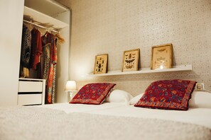 Une chambre à coucher avec un lit, des oreillers, une table de chevet, un miroir et une armoire.