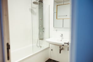 A bathroom with a glass-enclosed shower, a white sink, and a mirror with a gold frame. - Vrbo Property (Sevilla)