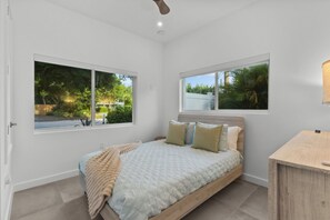 A bedroom with a bed, two windows, a ceiling fan, and a bedside table. - Modern 3BR • Private Backyard • Minutes to Downtown & Siesta Key (Sarasota)
