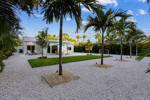 Ein modernes Haus mit Terrasse, Palmen und einem gepflegten Rasen.