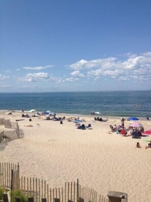 A beach with people sunbathing and swimming, a wooden fence, and a clear sky.