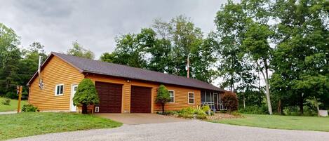 En envåningsstuga byggd av timmer, med en mörkbrun garageport, en veranda och en grusuppfart.
