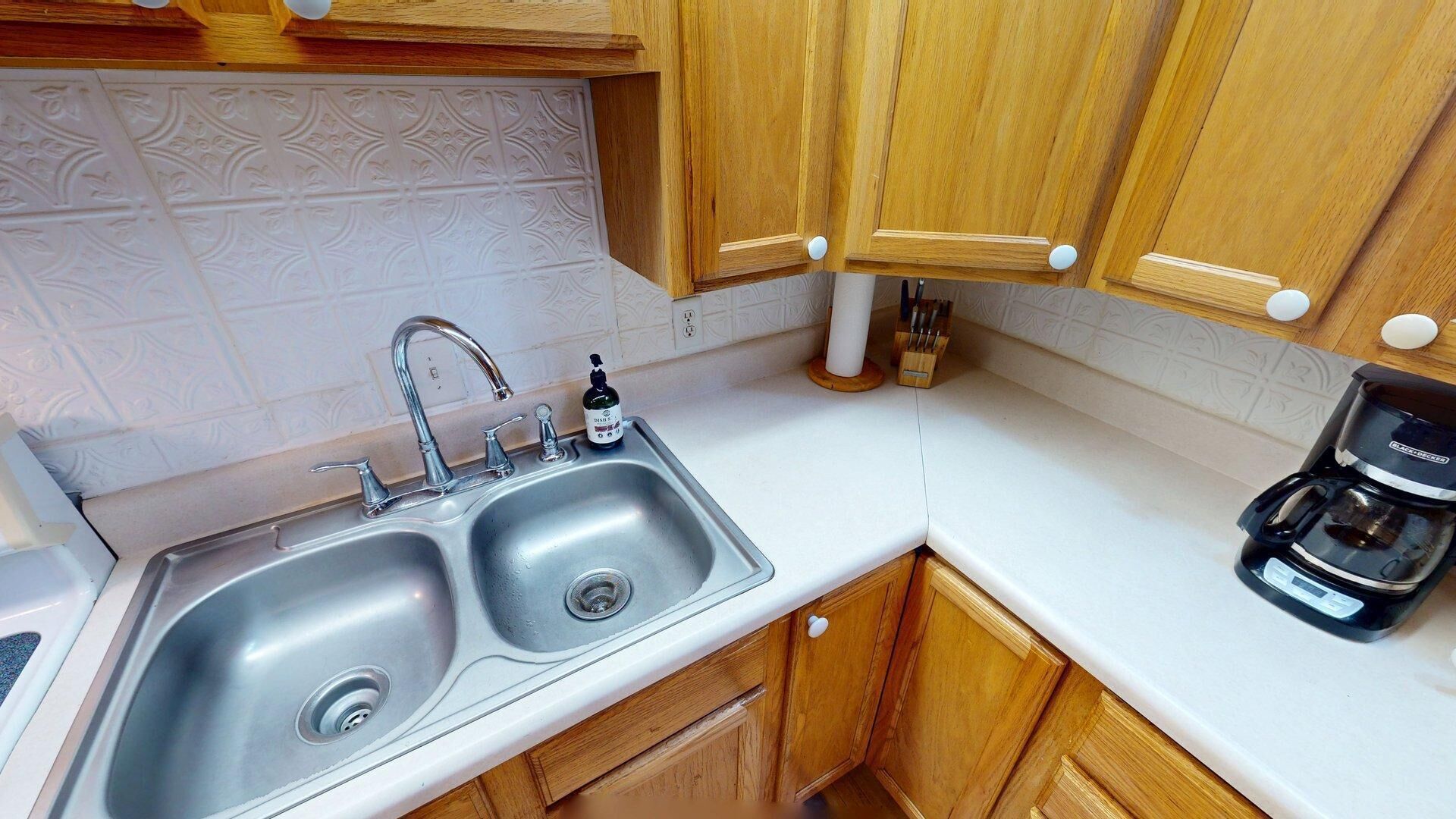 A kitchen with a double sink, wooden cabinets, a coffee maker, and a knife block.