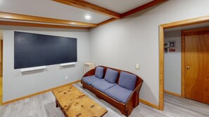 Ein Zimmer mit Holzboden, einem großen Flachbildfernseher an der Wand, einem Holzsofa mit Kissen und einem kleinen Holztisch.