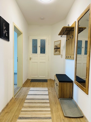 A hallway with a wooden floor, a striped rug, a door with frosted glass panels, a mirror, and a small wooden cabinet.