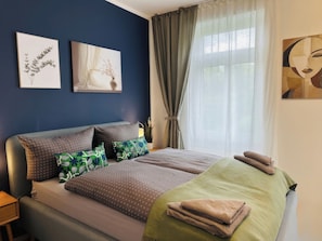 A neatly made bed with patterned bedding, a bedside lamp, and artwork on the walls. - Stylish 2BR apartment (Leipzig)