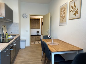 A modern kitchen with a wooden table and chairs, a clock, and framed artwork on the wall. - Stylish 2BR apartment (Leipzig)