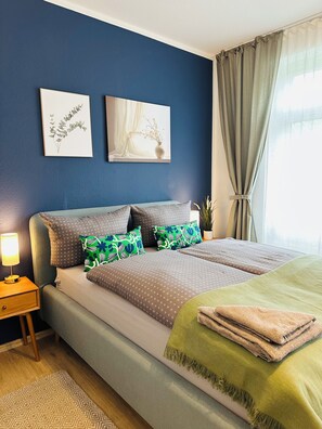 Een slaapkamer met een bed, kussens, een nachtkastje, een lamp en kunst aan de muur.