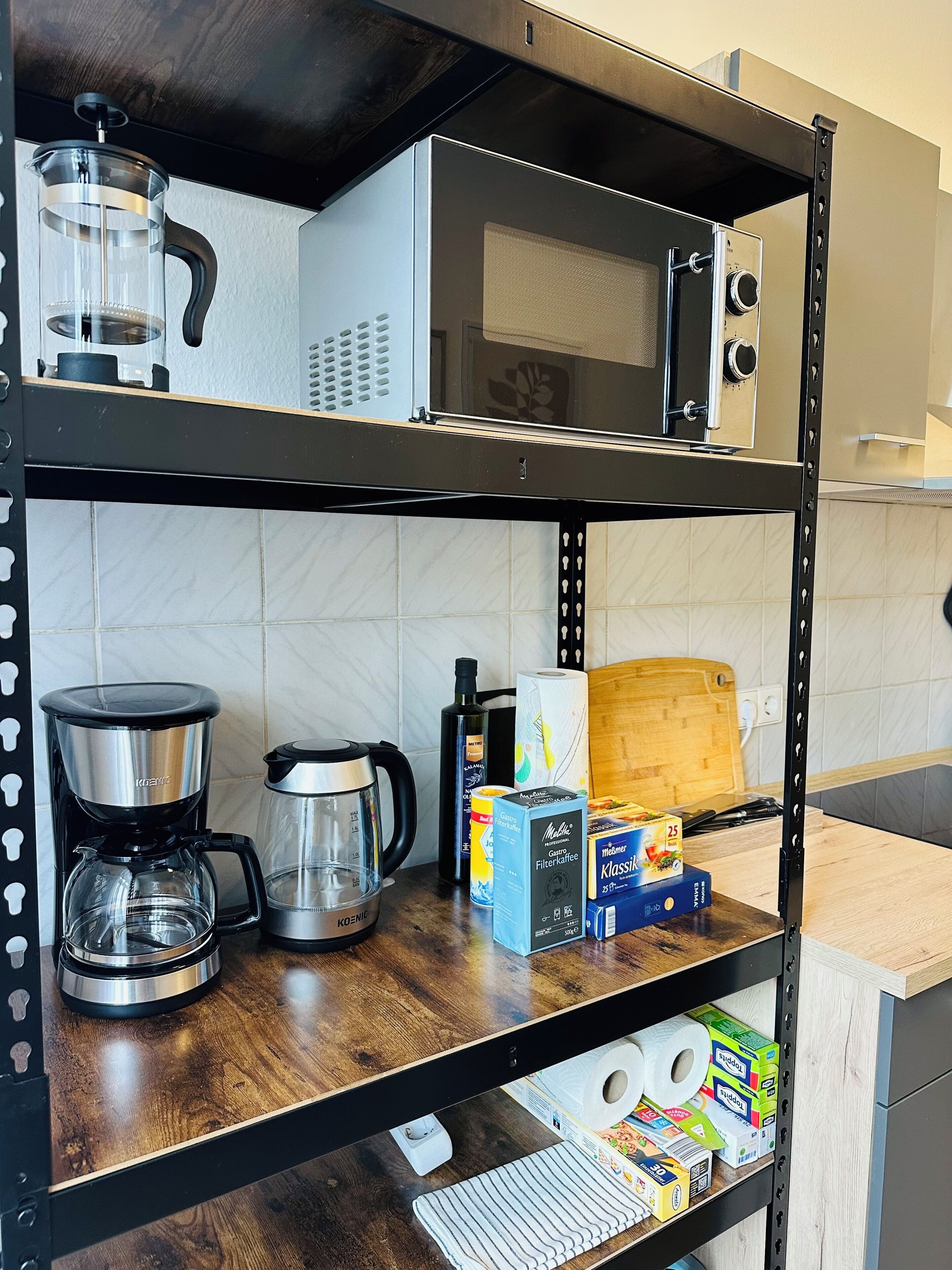 Ein Küchenregal mit einer Kaffeemaschine, einem Wasserkocher und verschiedenen Küchenutensilien.