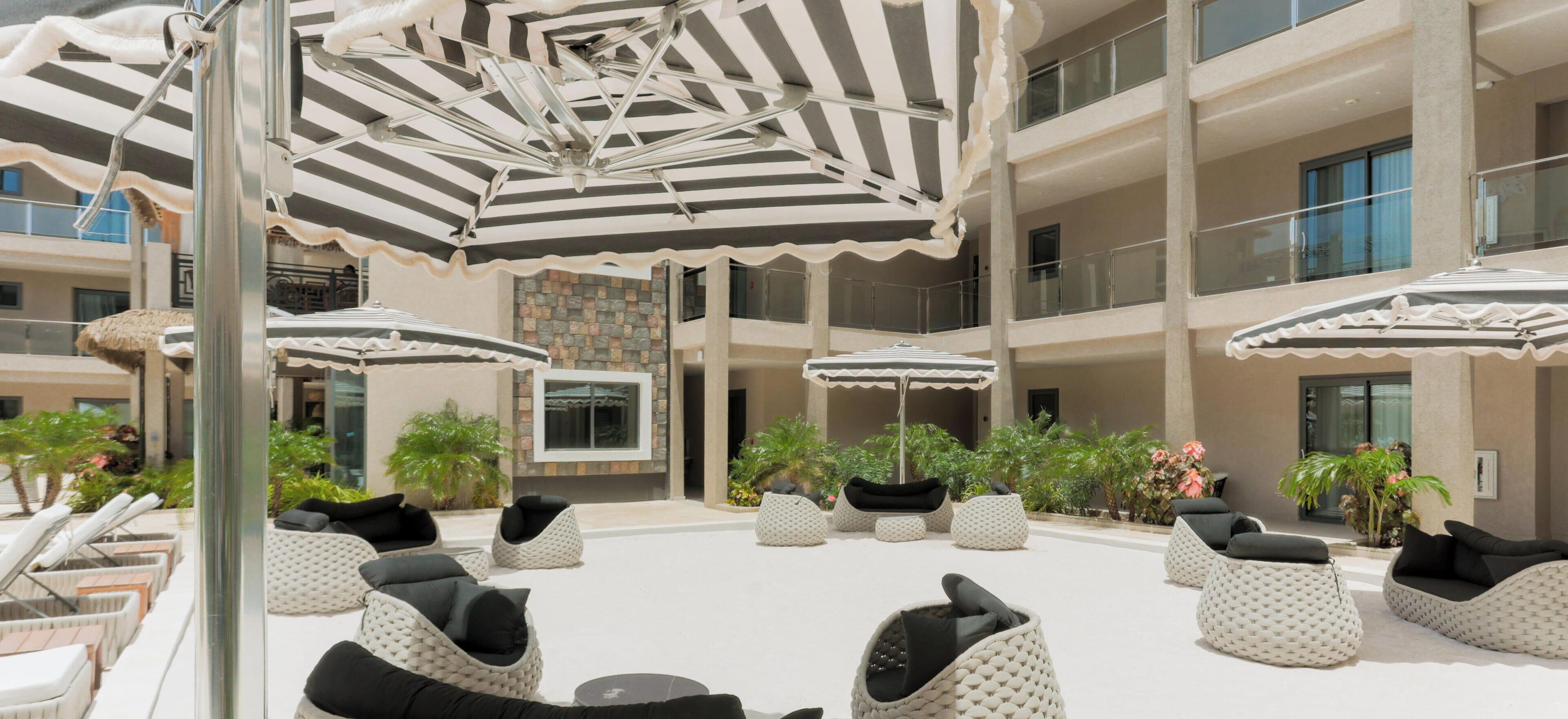 A spacious outdoor seating area with multiple lounge chairs and umbrellas, surrounded by a building with balconies and large windows.