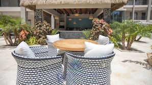 An outdoor seating area with a round wooden table and wicker chairs, surrounded by decorative plants and a patterned wall. - Brand New Luxury Condo Near Eagle Beach-Pool & Gym, Walishali Condos (Oranjestad)