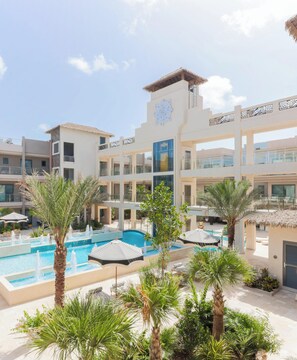 A hotel with a swimming pool, palm trees, and a modern architectural design. - Brand New Luxury Condo Near Eagle Beach-Pool & Gym, Walishali Condos (Oranjestad)