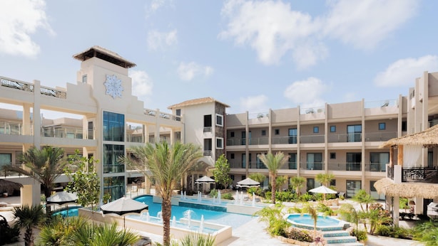 A hotel with multiple balconies, a central swimming pool, and tropical landscaping. - Brand New Luxury Condo Near Eagle Beach-Pool & Gym, Walishali Condos (Oranjestad)