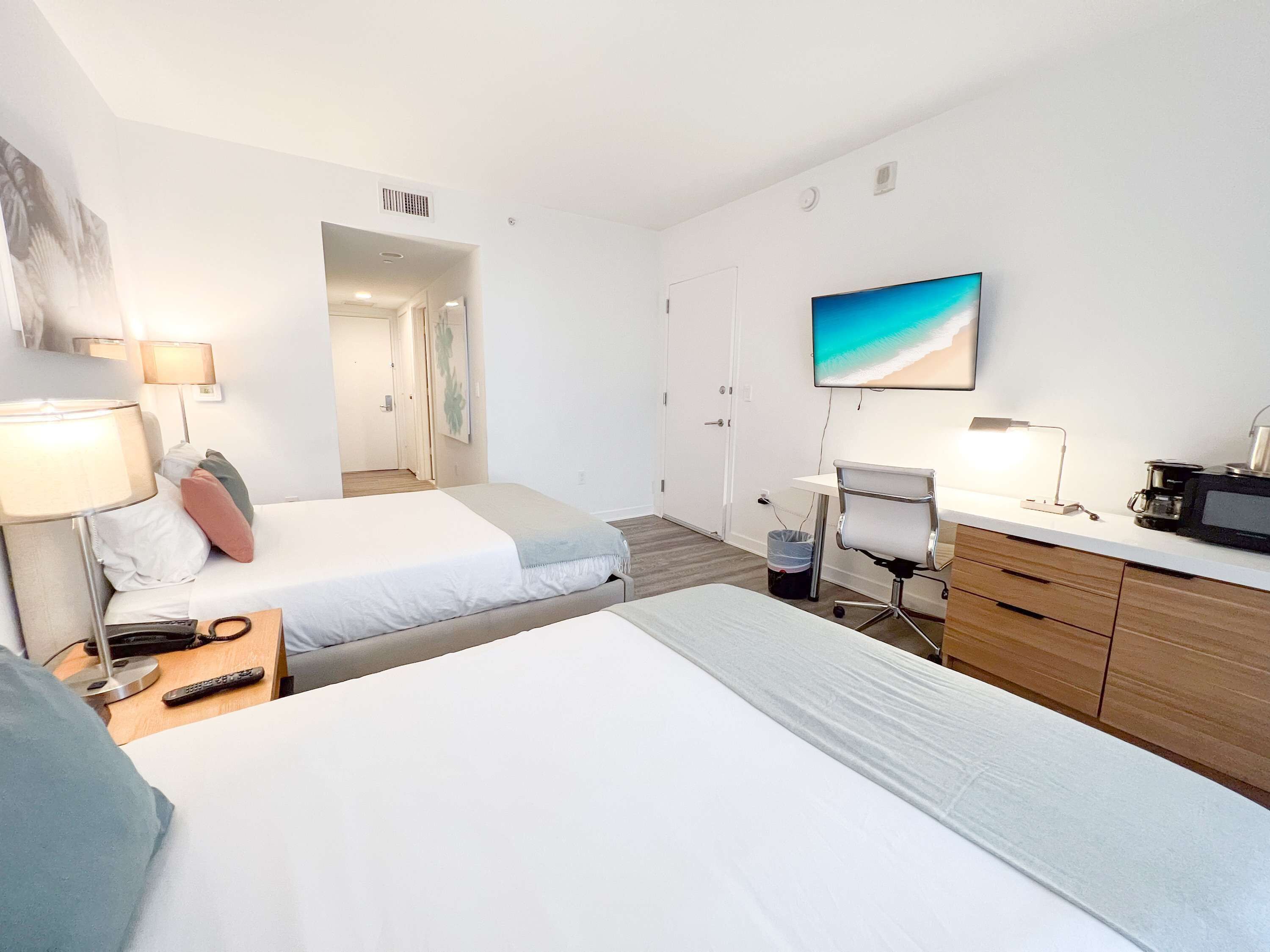 A hotel room with two beds, a desk, a chair, a TV, and a coffee maker.
