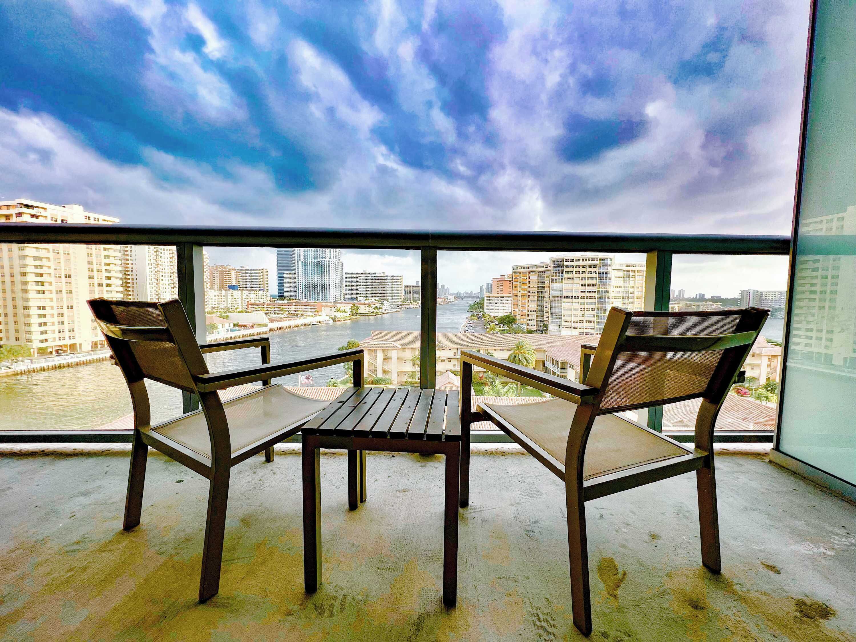 A balcony with two chairs and a table, overlooking a river and cityscape.