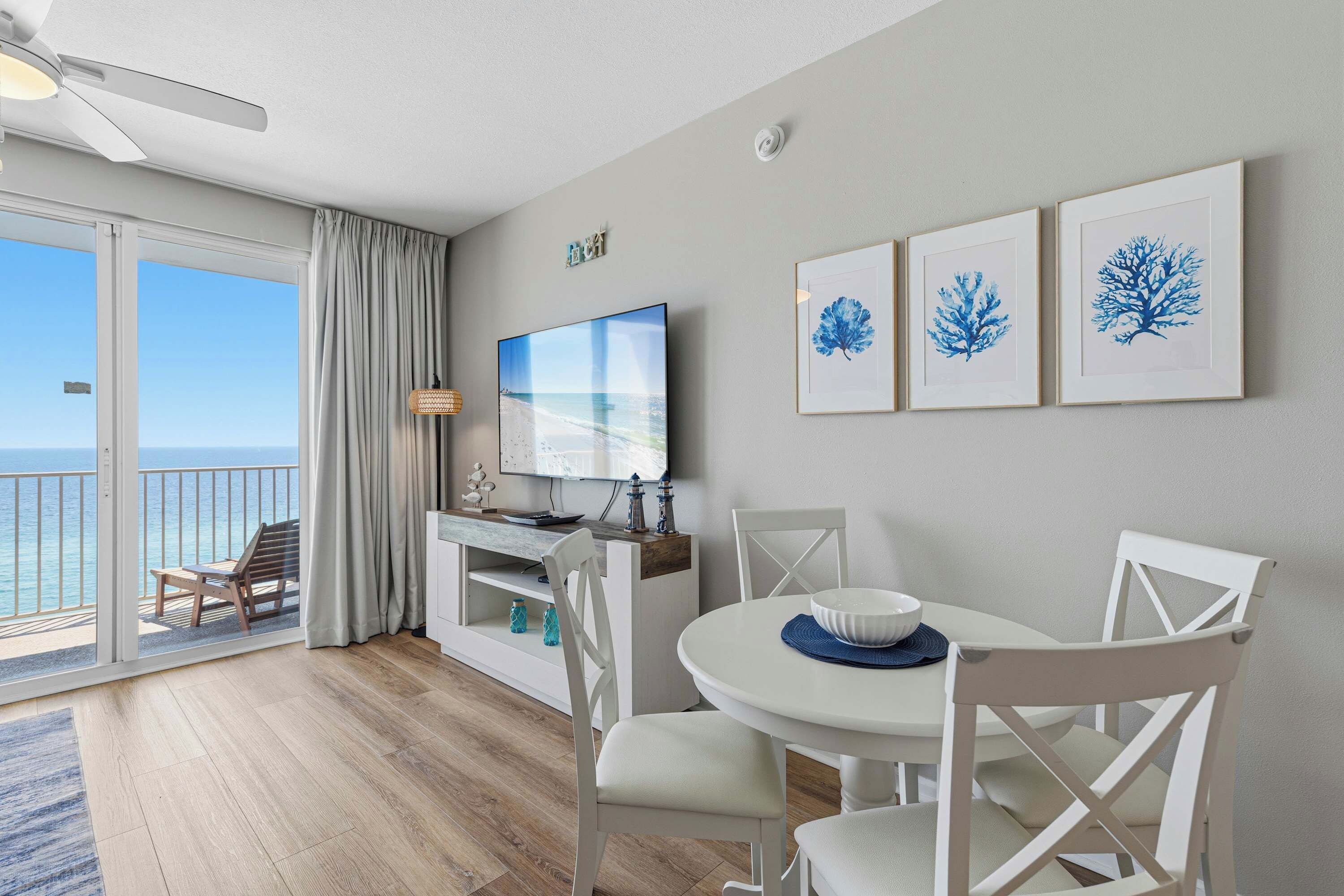 Un salon moderne doté d’une grande télévision, d’une table à manger avec des chaises et d’un balcon offrant une vue sur la mer.