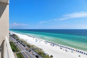 Ein Strand mit einer parallel zur Küste verlaufenden Straße, blauem Himmel und ruhiger See.