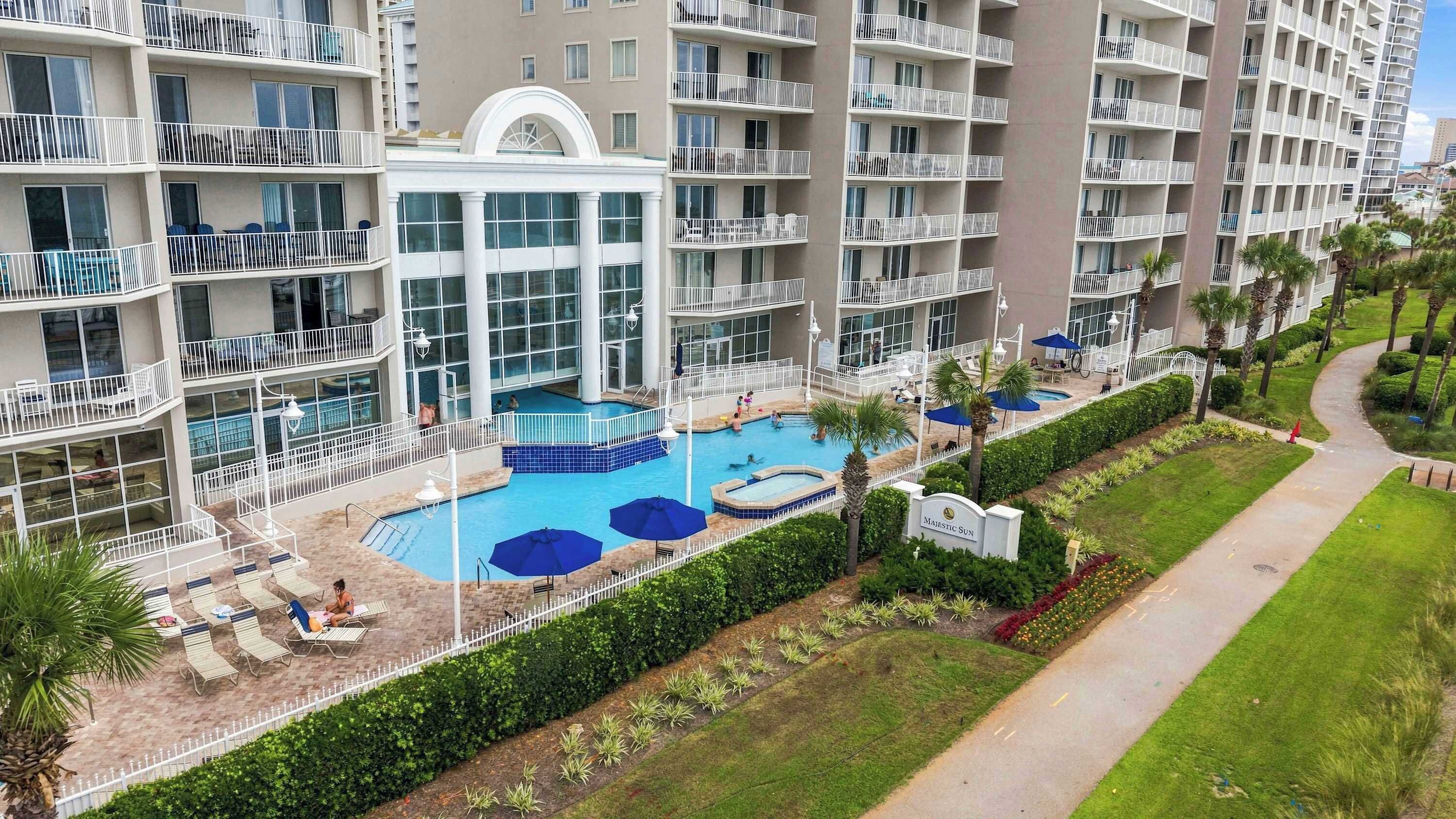 Un hôtel à plusieurs étages doté d’une piscine centrale, d’un espace extérieur aménagé et d’un jardin bien entretenu.