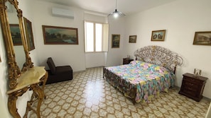 Ein Schlafzimmer mit einem Bett, einem Sessel, einem Schminktisch, einem Spiegel und einem Fenster.