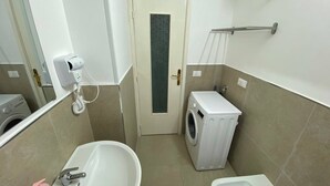 Uma casa de banho compacta com máquina de lavar roupa, banheira e sanita.