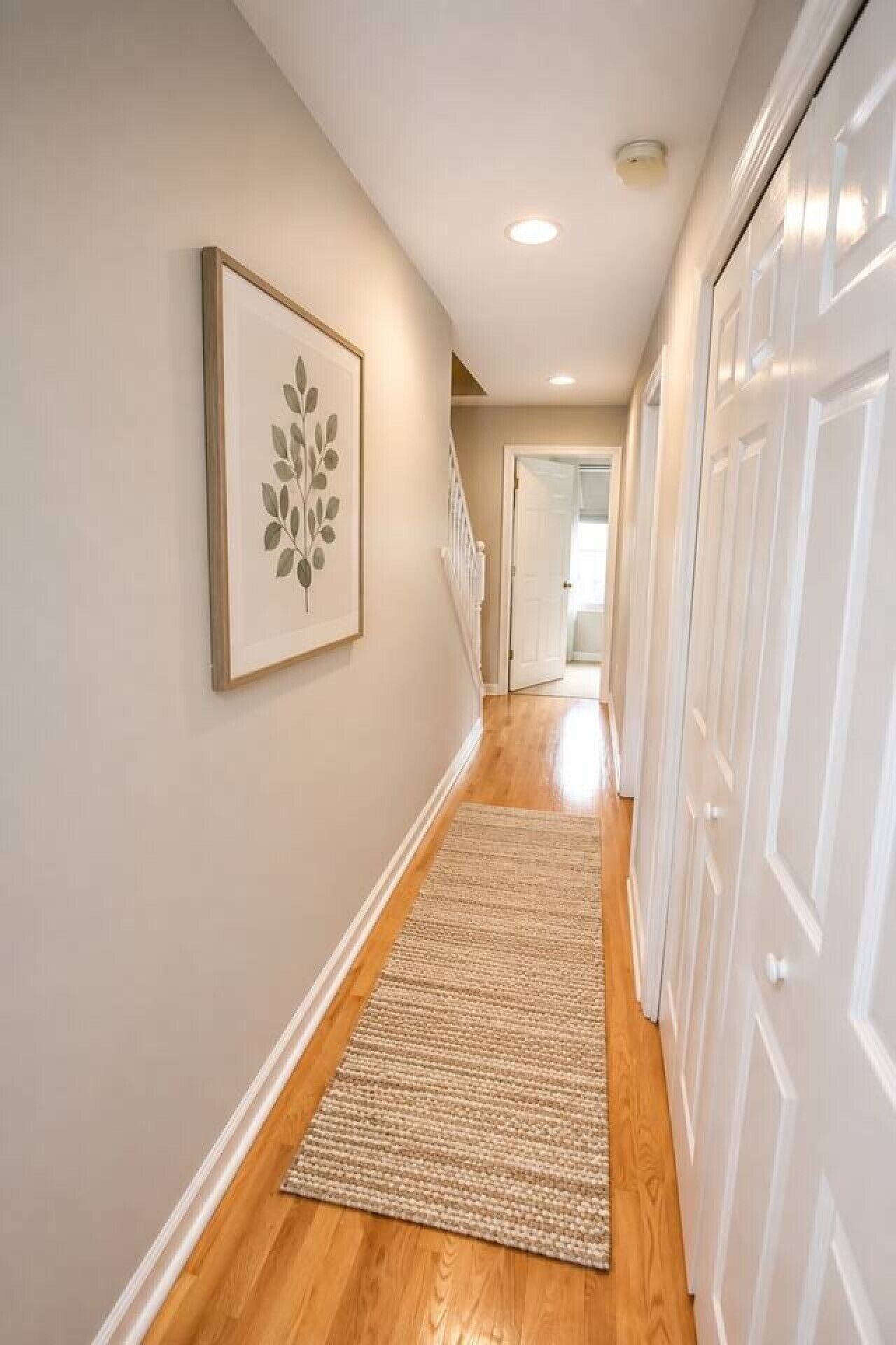 A hallway with a wooden floor, a rug, and a framed picture on the wall.